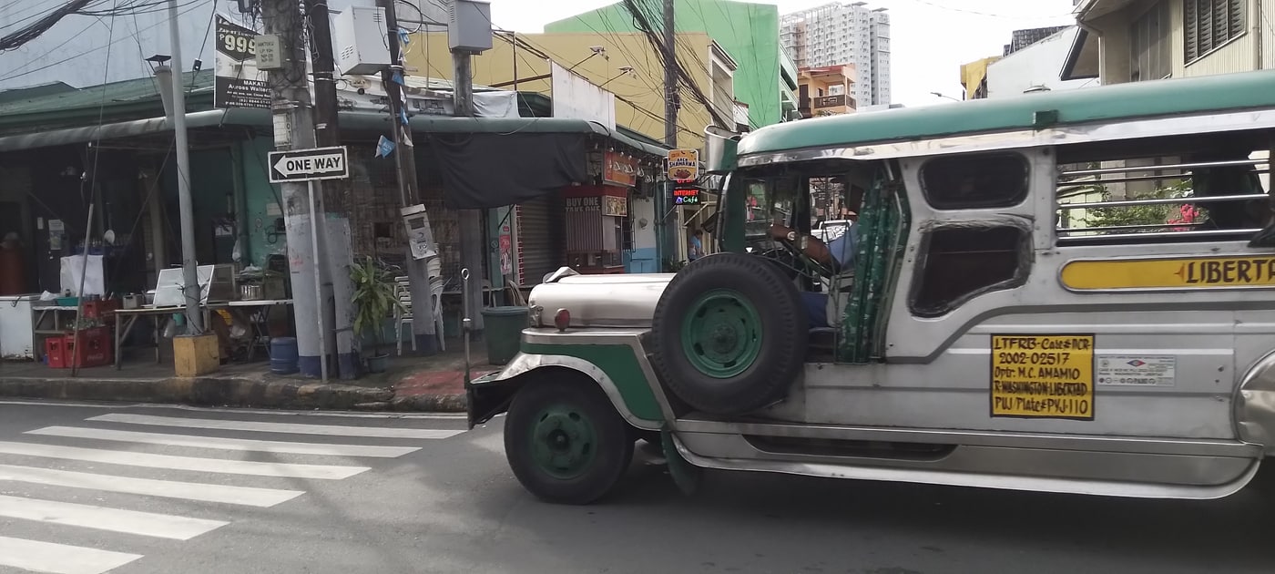 A jeepney — the Philippines' iconic shared-ride vehicle — on a Manila street, with local shops, overhead wires and a one-way sign