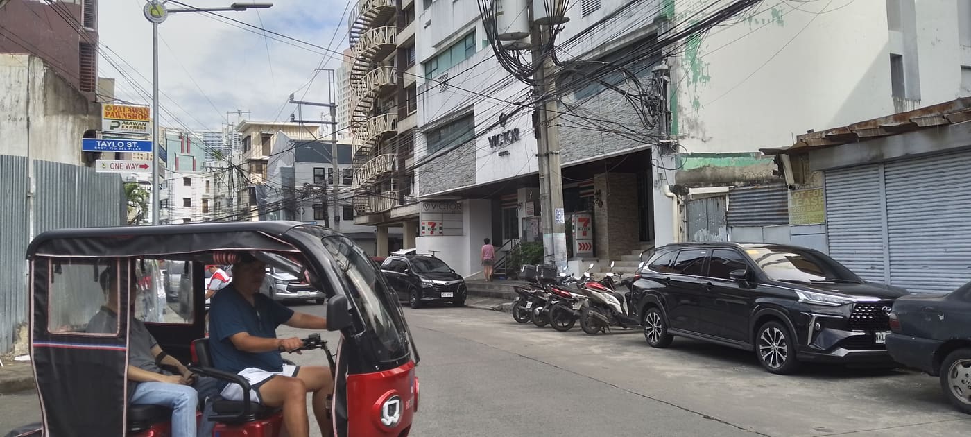 A tricycle (a covered three-wheeled taxi) on a Manila street near Taylo St., with motorbikes, cars, a convenience store and a pawnshop sign